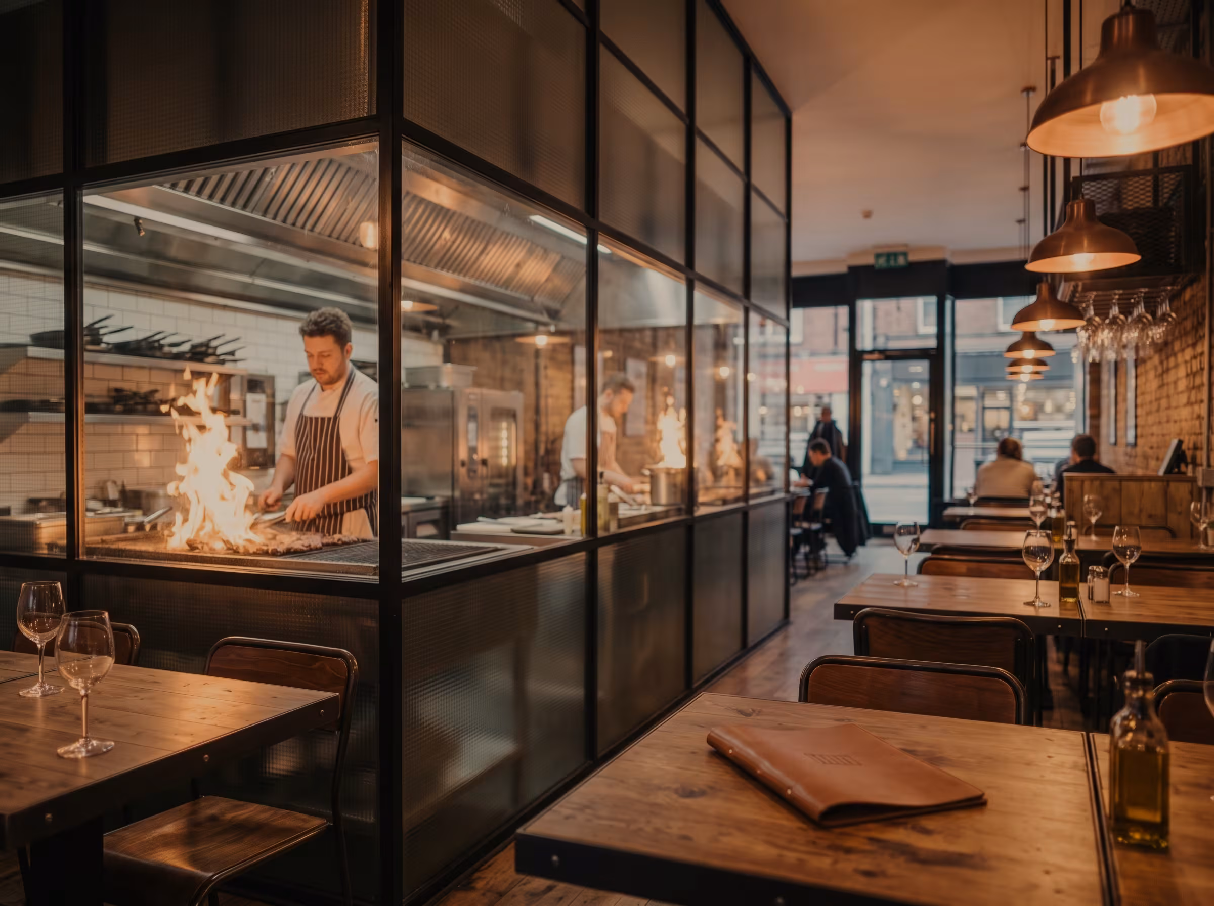 The dining room, with a cook at the grill behind the glass wall of the open kitchen.